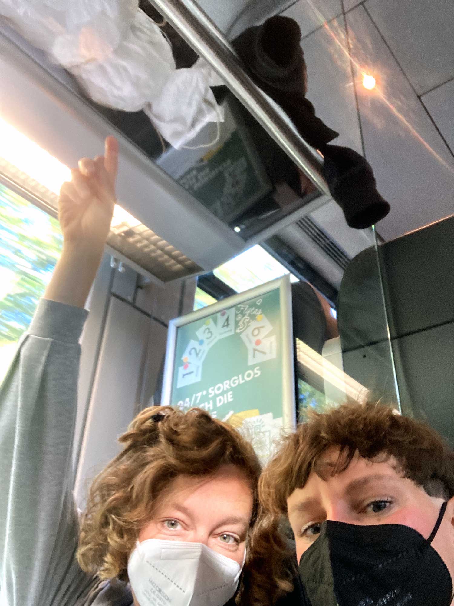 Zwei Frauen in einem Zug mit dem Zeigefinger auf die Hutablage gerichtet,