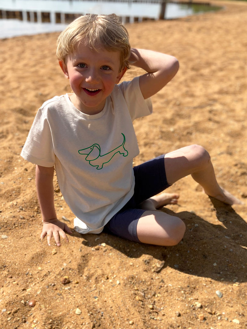 Kind sitzt am Strand in Biobaumwollshirt von RUDIS